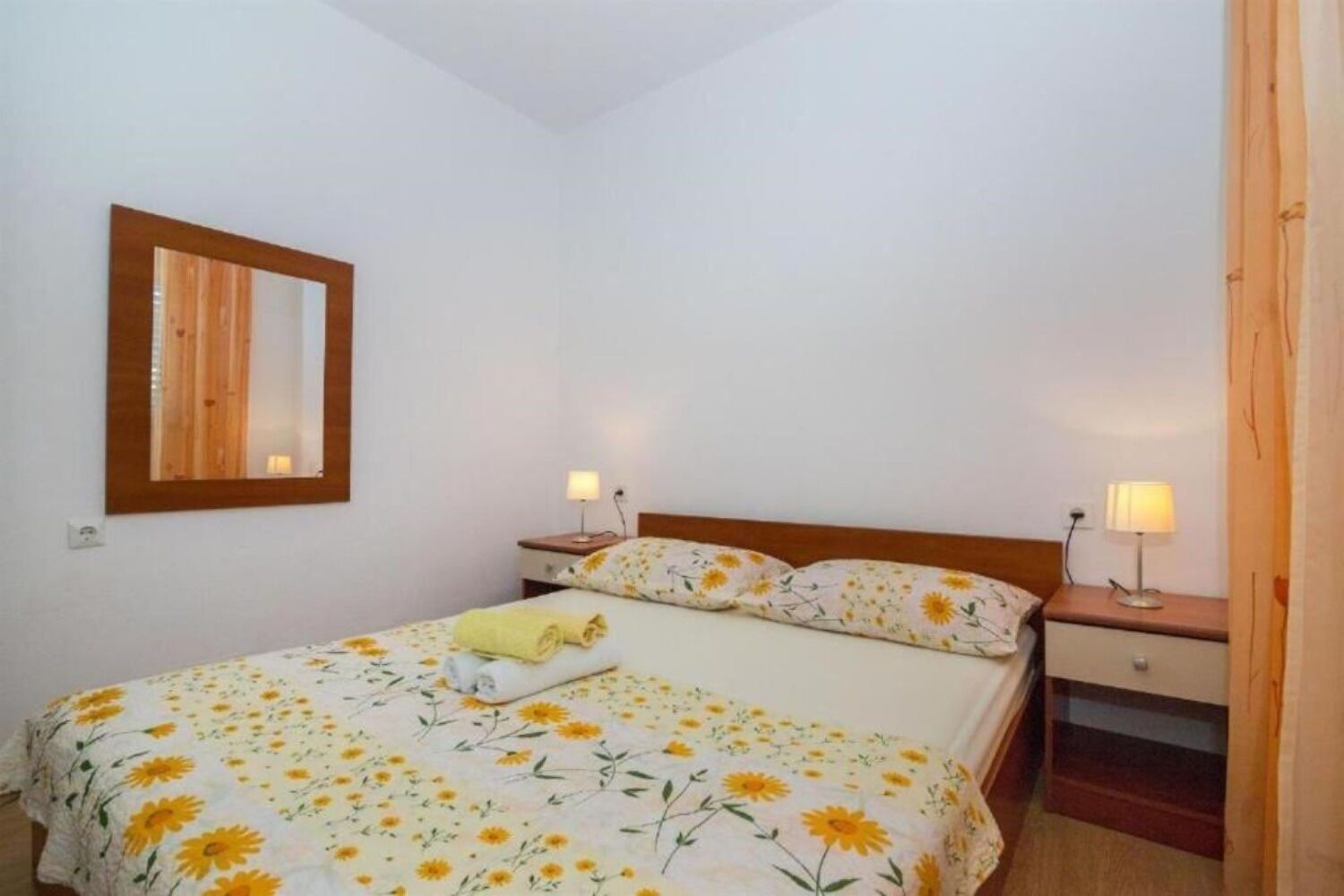 Un dormitorio con una cama, dos mesitas de noche, un espejo y una lámpara a cada lado.