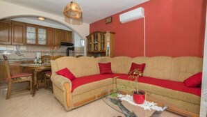 A living room with a beige sofa, red cushions, a glass coffee table, and a dining area with wooden furniture. - Apartments Mari (Marina)