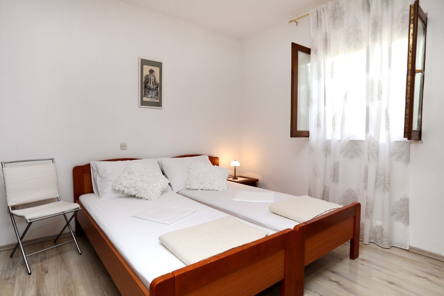 Un letto matrimoniale con lenzuola bianche, una lampada da comodino e una sedia.