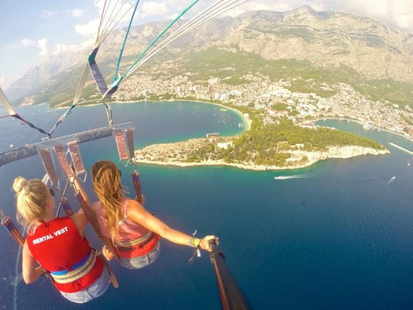 Vista aérea deslumbrante de uma cidade costeira, com mar azul cristalino e montanhas ao fundo.
