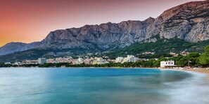 A coastal town with buildings along the waterfront, a mountain backdrop, and a clear view of the sea. - Apartment Stipe (Makarska)