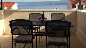 A terrace with a table and four chairs, overlooking a body of water and distant hills. - Apartment Nikola M (Bol)