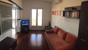 A living room with a wooden floor, a sofa, a television, a bookshelf, and a door leading outside. - Apartment Nikola M (Bol)