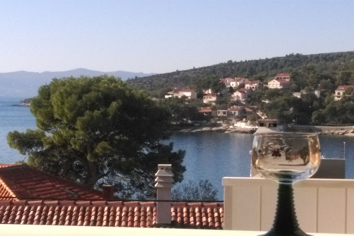 A coastal view with a glass on a balcony, overlooking a village with houses and a body of water.