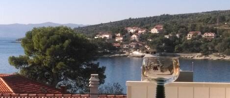 A coastal view with a glass on a balcony, overlooking a village with houses and a body of water.