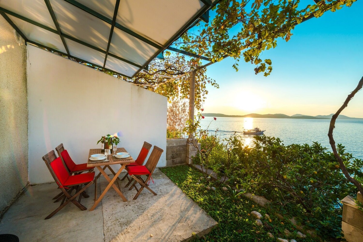 Uma área de refeições ao ar livre com uma mesa e cadeiras, com vista para um corpo d'água e um barco ao longe.
