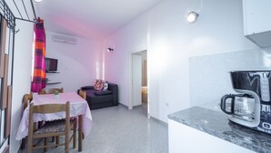 Et kompakt køkken med kaffemaskine, spiseplads med bord og stole, samt en sofa.