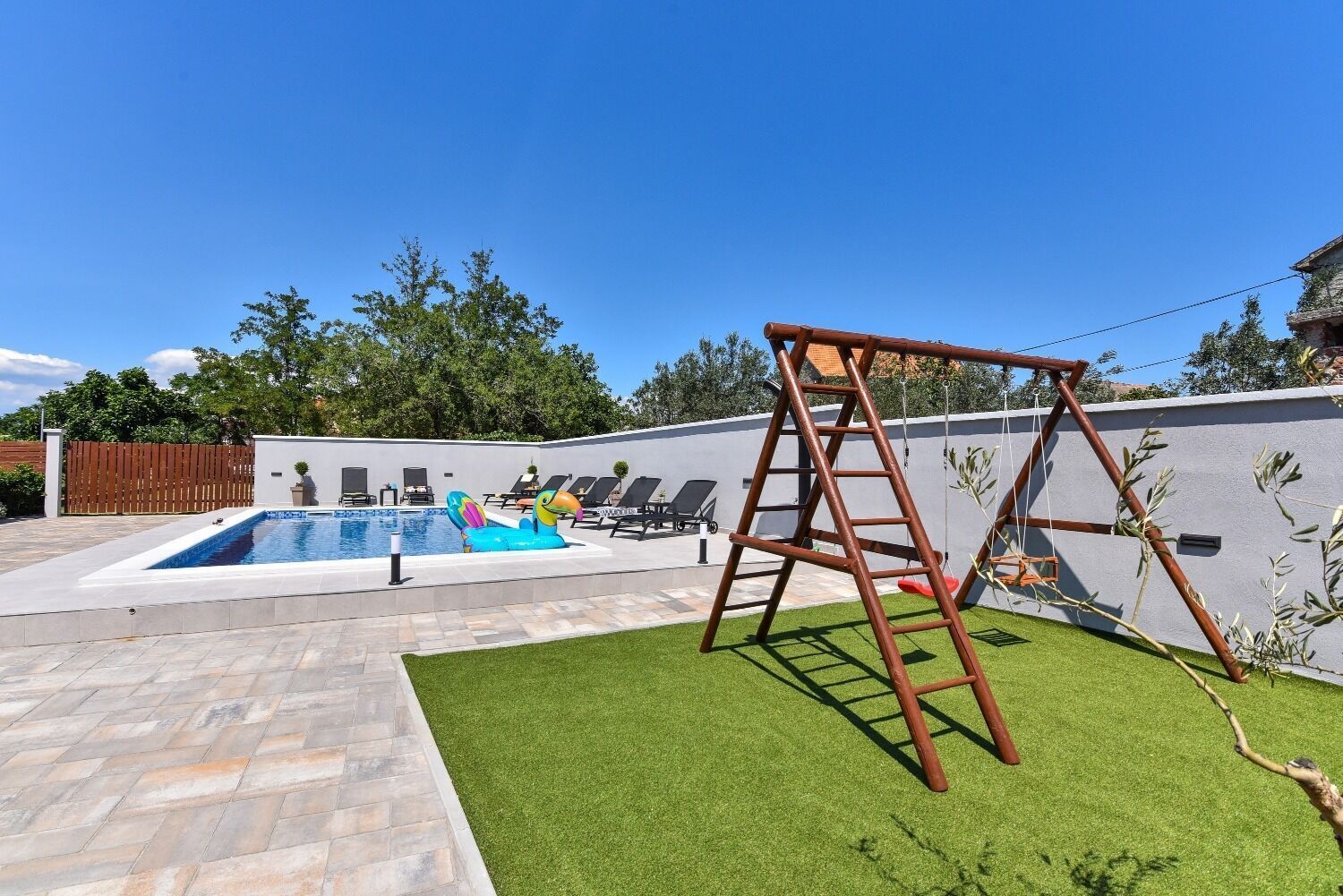 A backyard with a swimming pool, a swing set, and a grassy area.
