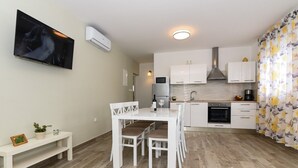 Eine moderne Küche mit weißen Schränken, einem eingebauten Backofen und einer Mikrowelle. Es gibt einen Essbereich mit einem weißen Tisch und Stühlen, sowie eine Bank mit einem Blumentopf.
