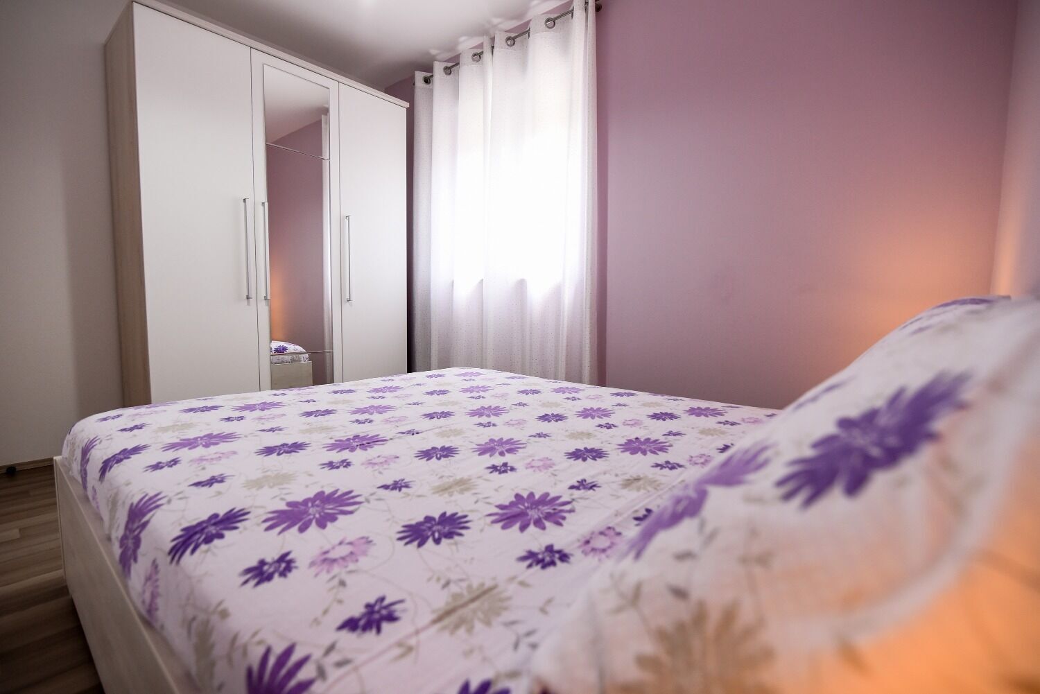 A bedroom with a bed, a wardrobe, and a window with curtains.