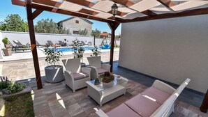 Ein überdachter Außenbereich mit Korbmöbeln und einem Pool im Hintergrund.