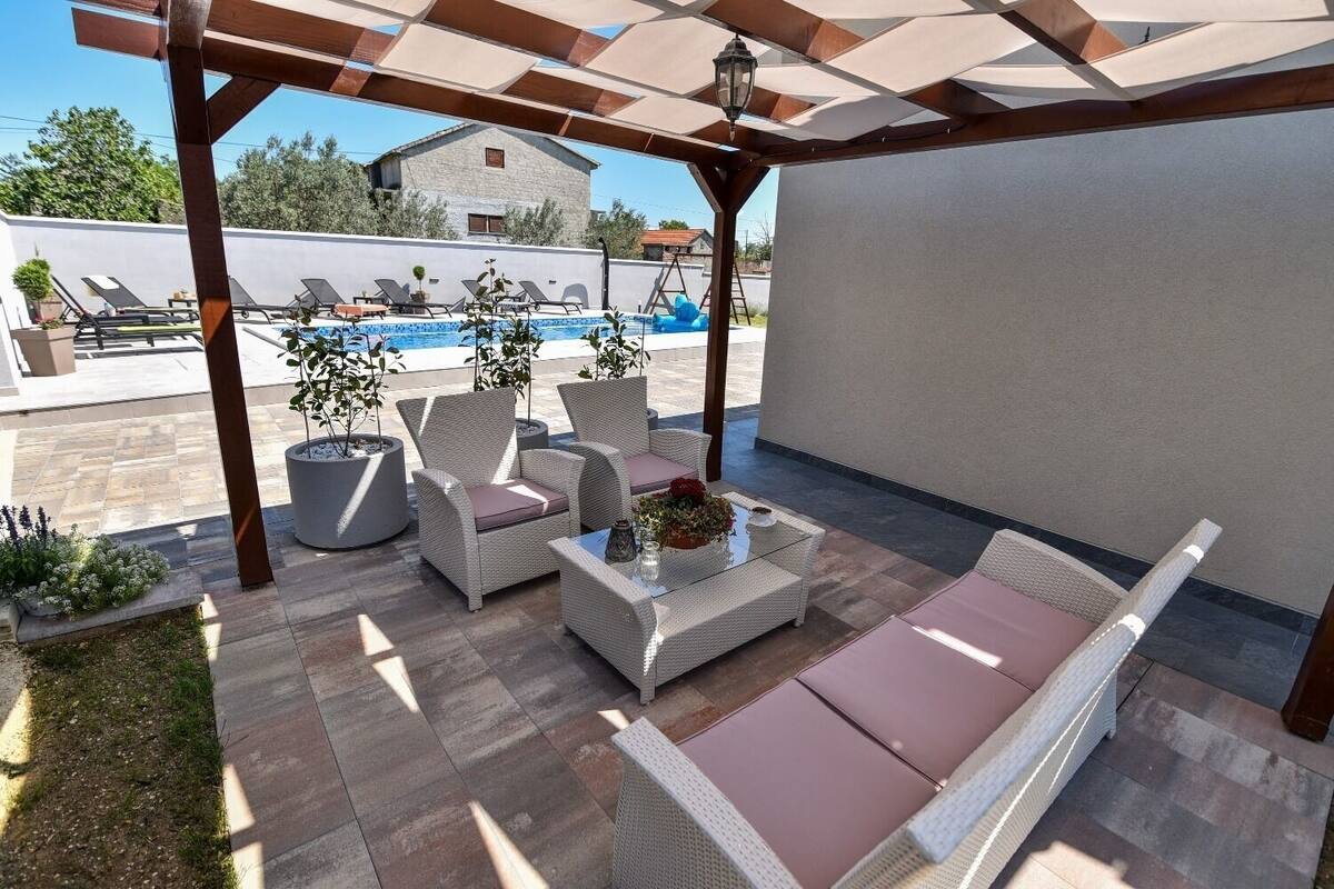 A covered outdoor seating area with wicker furniture and a pool in the background.