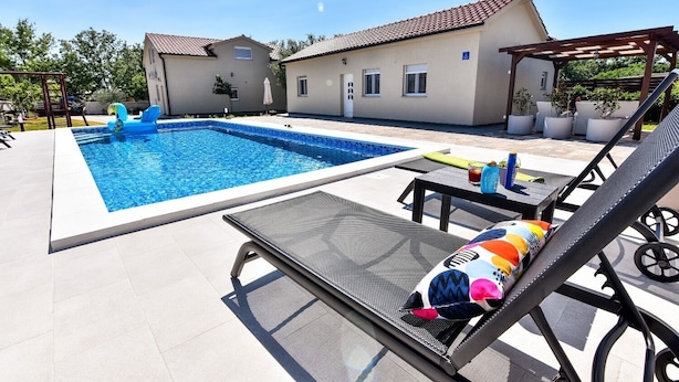 Ein Swimmingpool mit Liegestühlen und einer Pergola, umgeben von einem Haus mit einem Ziegeldach.
