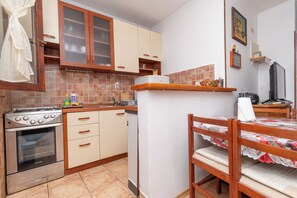 A compact kitchen with a stove, oven, and wooden cabinets. - Apartment Jakov (Okrug)