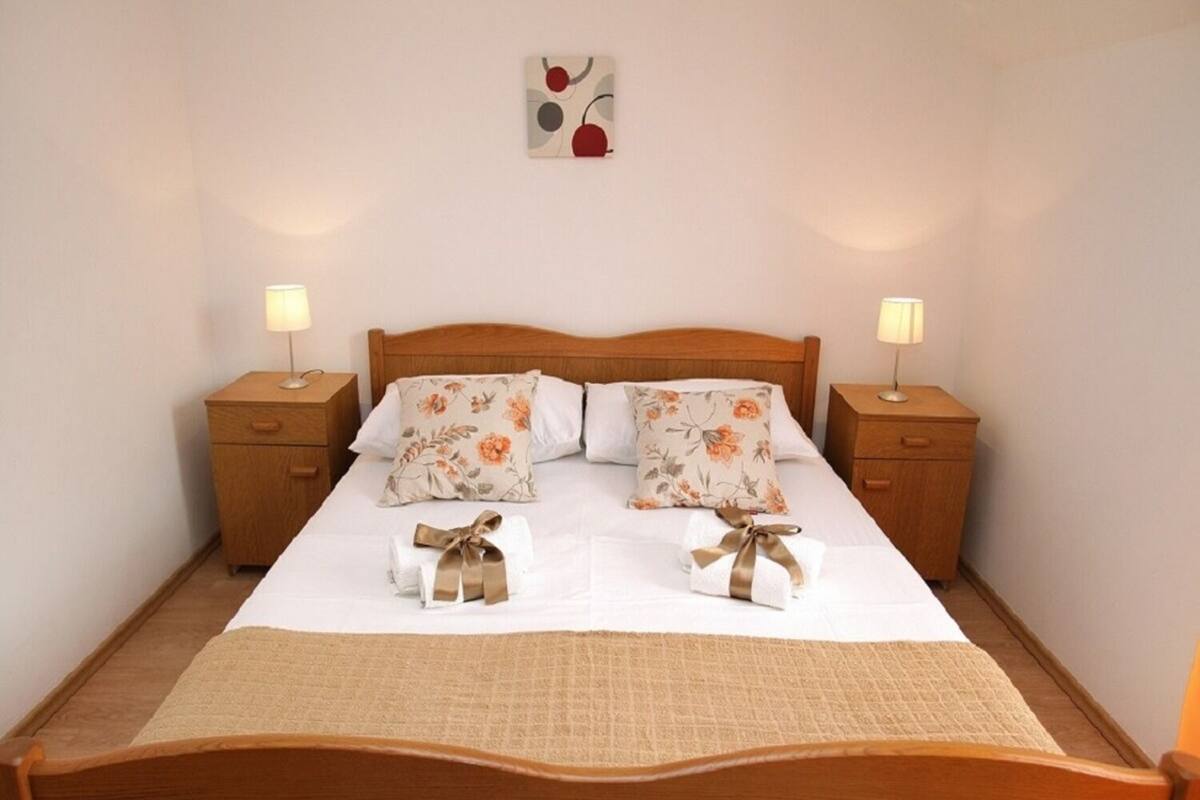 A neatly made bed with floral pillows, two bedside tables with lamps, and a wall art piece above the bed.