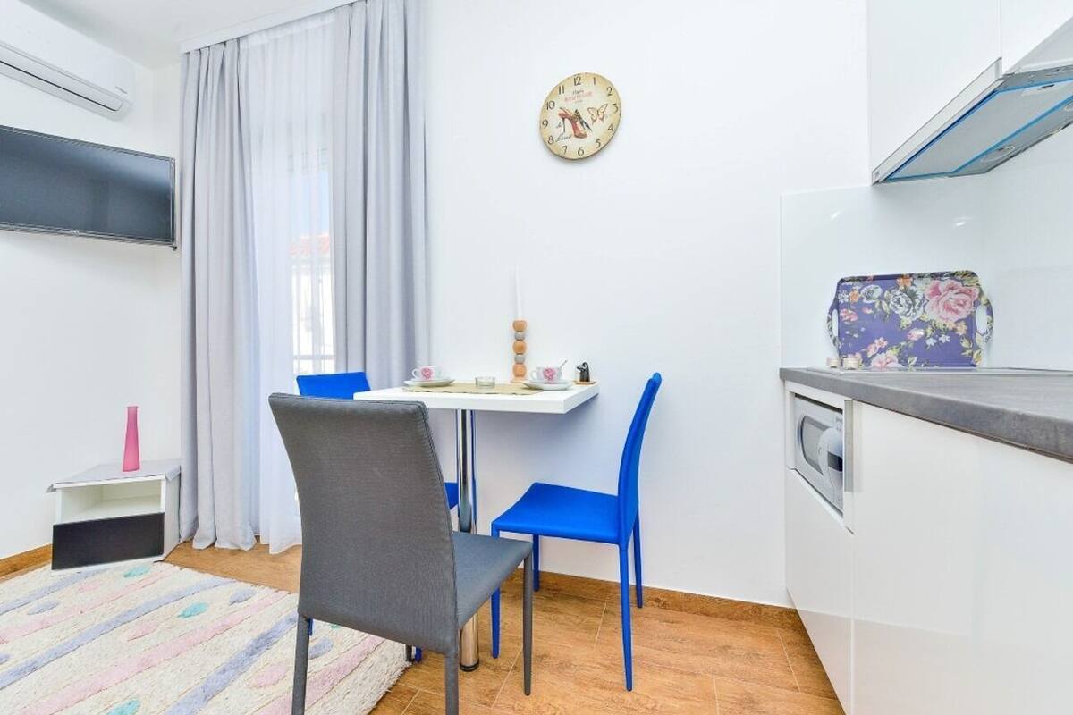 A compact kitchen with a dining table, chairs, a clock, and a microwave.