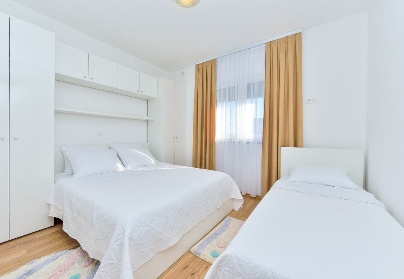 Une chambre avec deux lits, du linge de lit blanc, un plancher en bois et une grande fenêtre avec des rideaux.