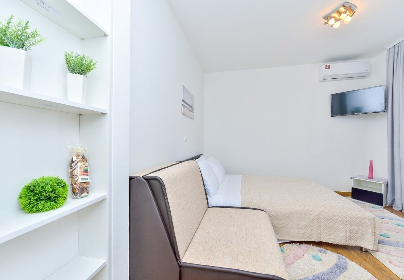 Een kleine slaapkamer met een bed, een nachtkastje, een televisie en een plank met planten en een decoratief object.