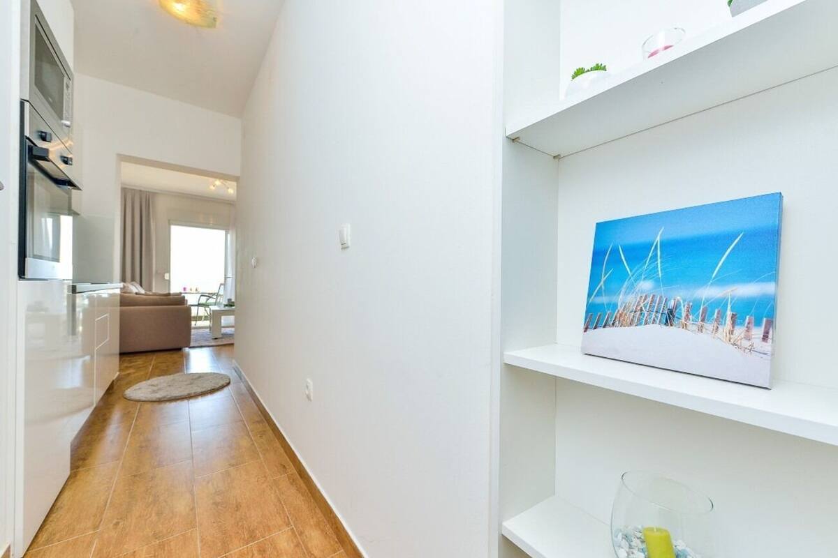 A modern kitchen with white cabinets, a built-in oven, and a dining area with a beige sofa.
