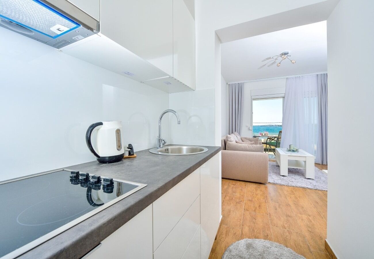 Cocina moderna con estufa integrada, lavamanos y hervidor. Cuenta con un comedor con sofá y vista al mar.