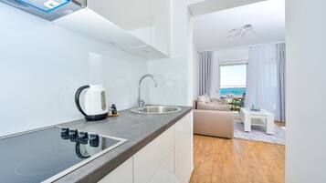 Cocina moderna con estufa integrada, lavamanos y hervidor. Cuenta con un comedor con sofá y vista al mar.