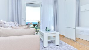 A modern living room with a sofa, a coffee table, and a view of the sea through a glass door. - Apartments Sunny by the Sea (Nin)