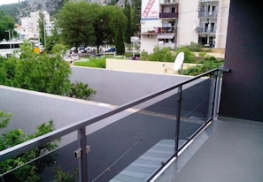 Un balcon doté d’une balustrade en verre, donnant sur un parking et des immeubles.