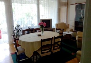 A dining area with a round table, chairs, a vase with flowers, a television, and a wardrobe. - House Marus (Omis)