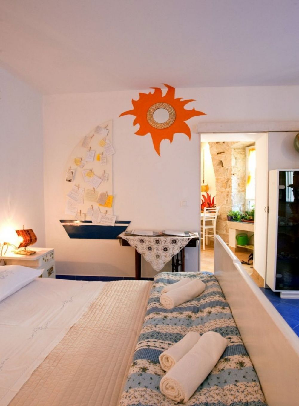 A bedroom with a bed, a desk, and a wall decorated with notes and a sun design.