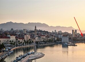 A coastal cityscape with a prominent tower, marina, and mountains in the background. - Apartment Happy (Split)