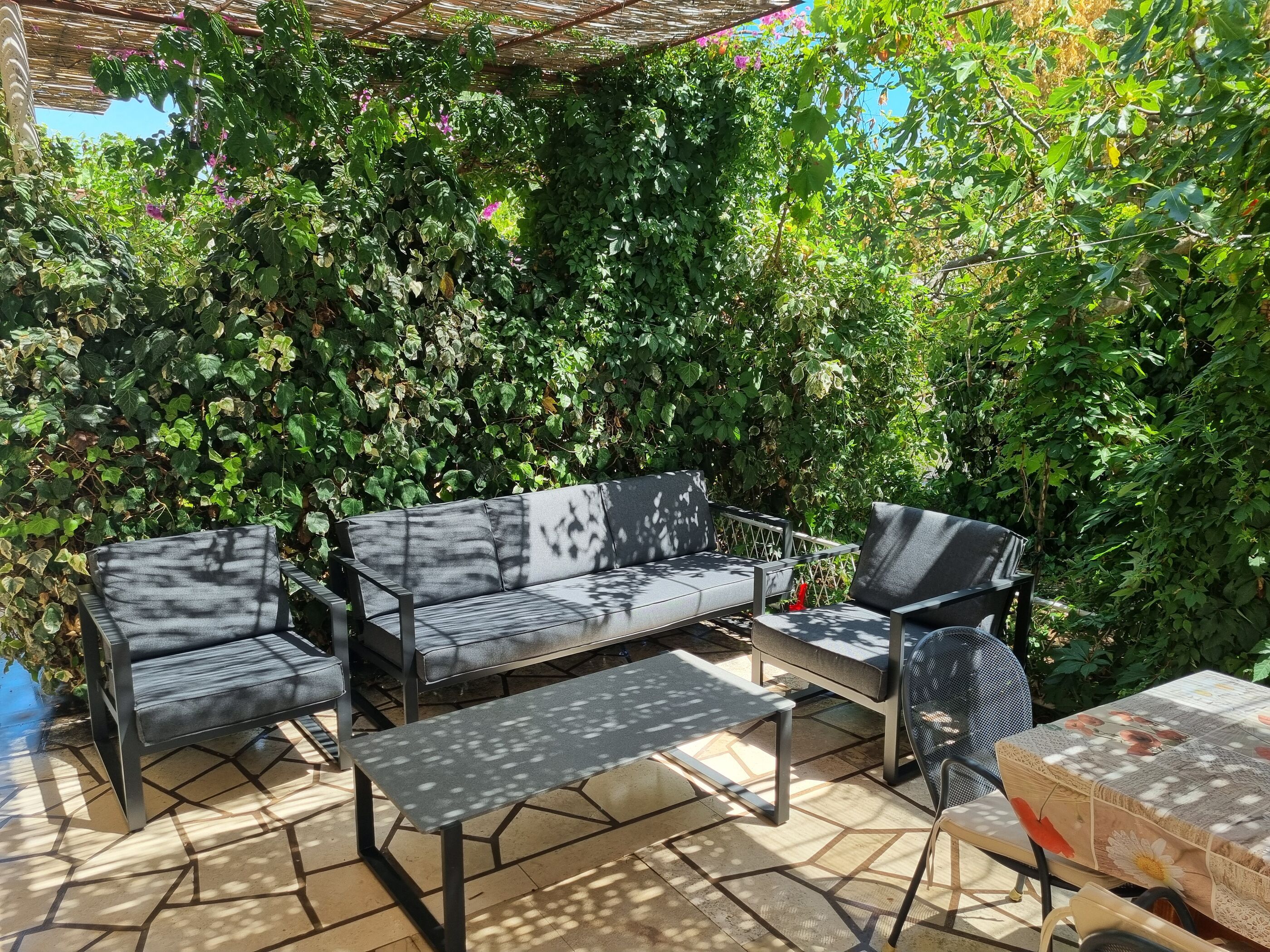 Un'area salotto esterna con divano, sedie e un tavolo, immersa nel verde.