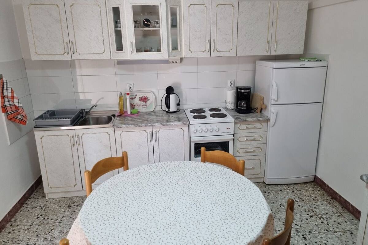 A compact kitchen with white cabinets, a stove, a refrigerator, and a dining table with chairs.