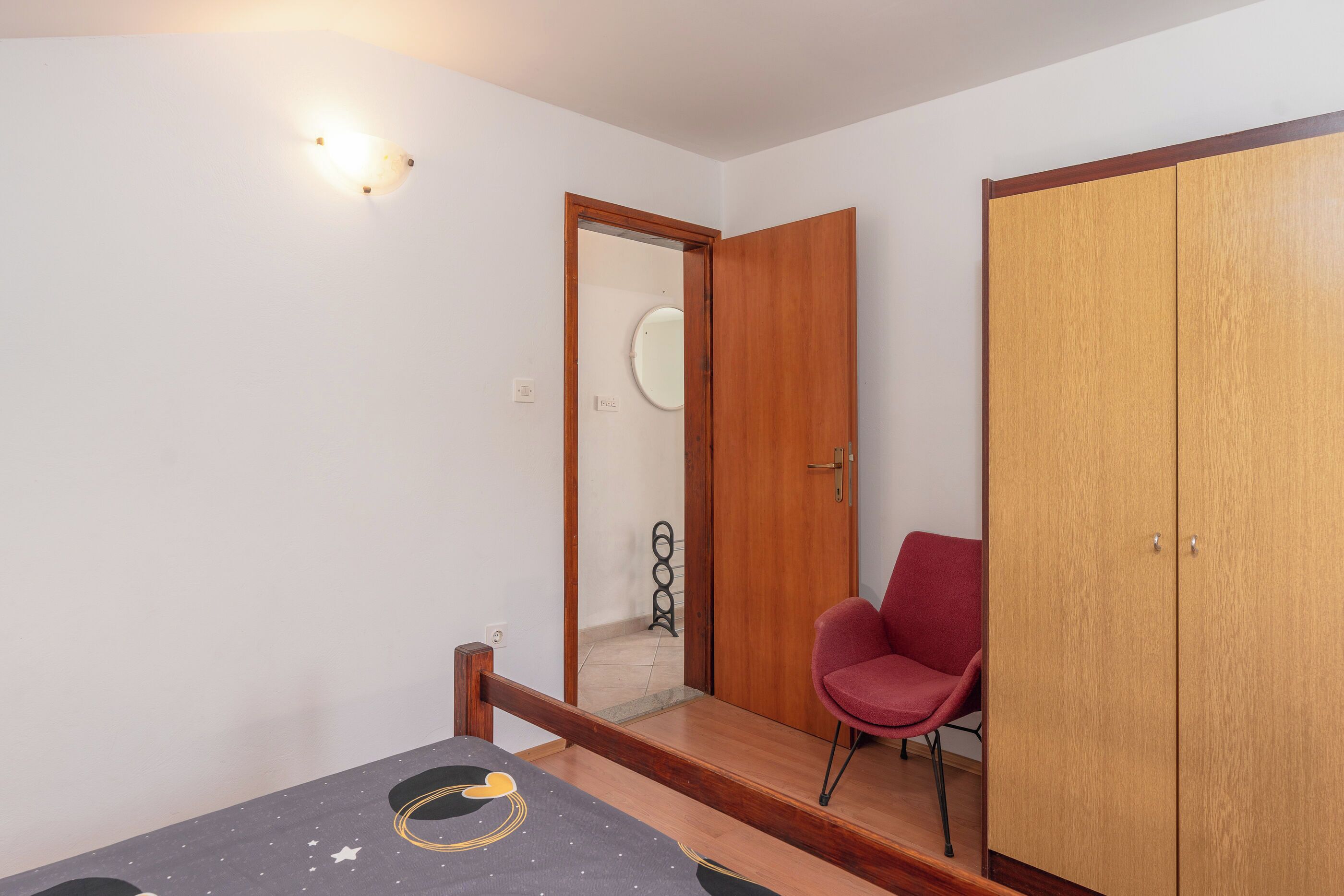 Ein Schlafzimmer mit einem Bett, einem Kleiderschrank, einem Sessel und einer Tür zu einem Badezimmer.