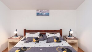 A bedroom with a wooden headboard, a bed with a star-patterned bedspread, two bedside tables with lamps, and a painting on the wall. - Apartments Darko (Vir)