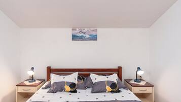 Quarto com cabeceira de madeira, cama com colcha estampada em formato de estrelas, duas mesas de cabeceira com luminárias e um quadro na parede.