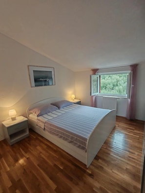 Ein Schlafzimmer mit einem Bett, Nachttischen, einem Fenster und einem gerahmten Bild an der Wand.