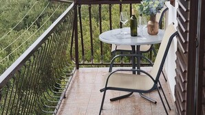 A balcony with a table and chairs, overlooking a body of water and greenery. - Apartment Damir (Tucepi)