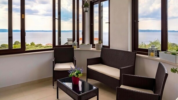 A balcony with wicker furniture, a glass table, and potted plants. - Apartment Damir (Tucepi)