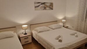 Een hotelkamer met twee bedden, elk voorzien van witte lakens en kussens, een klein nachtkastje met een lamp en een wanddecoratie.