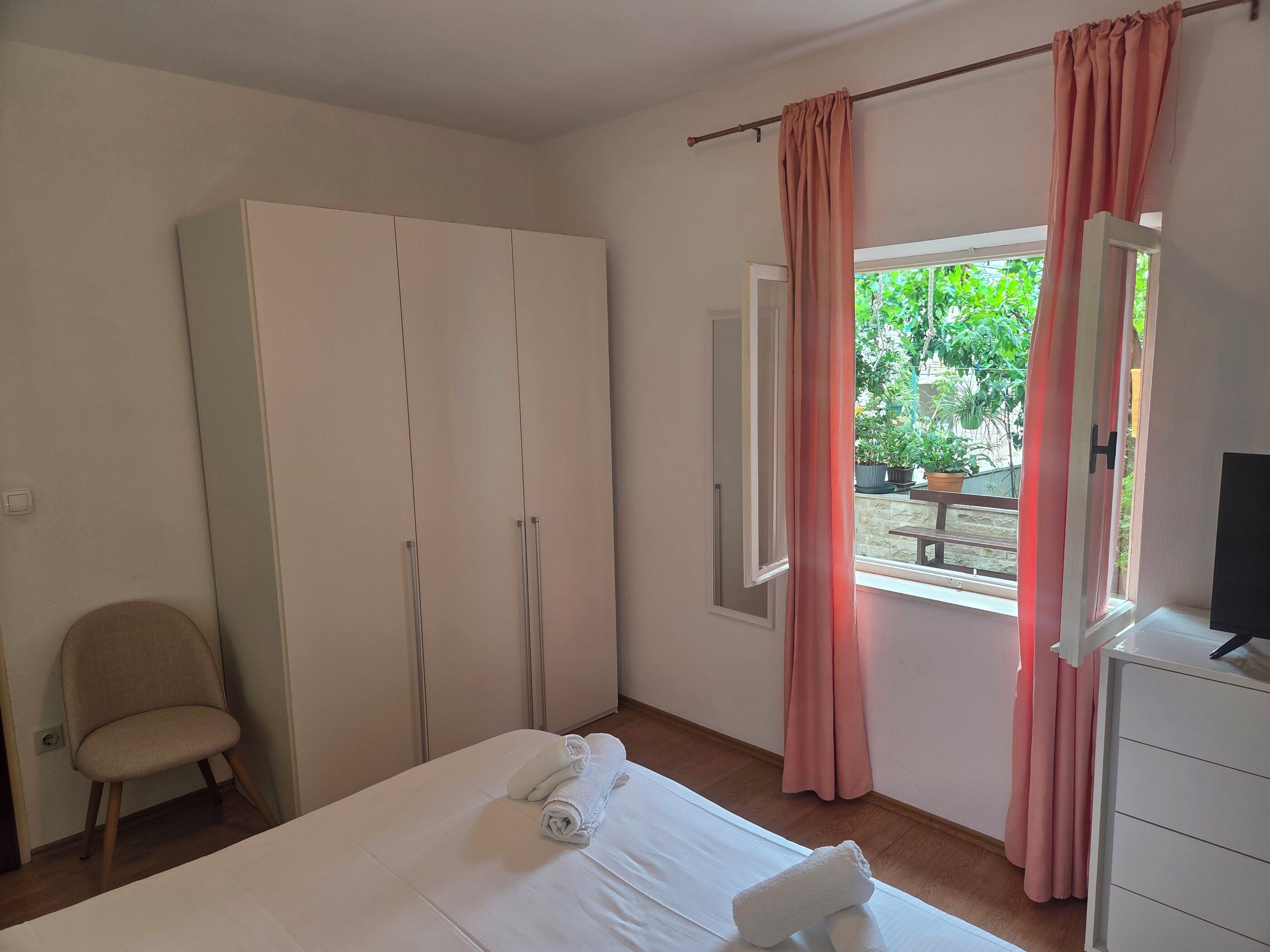 A bedroom with a bed, a wardrobe, a chair, a desk, and a window with curtains.