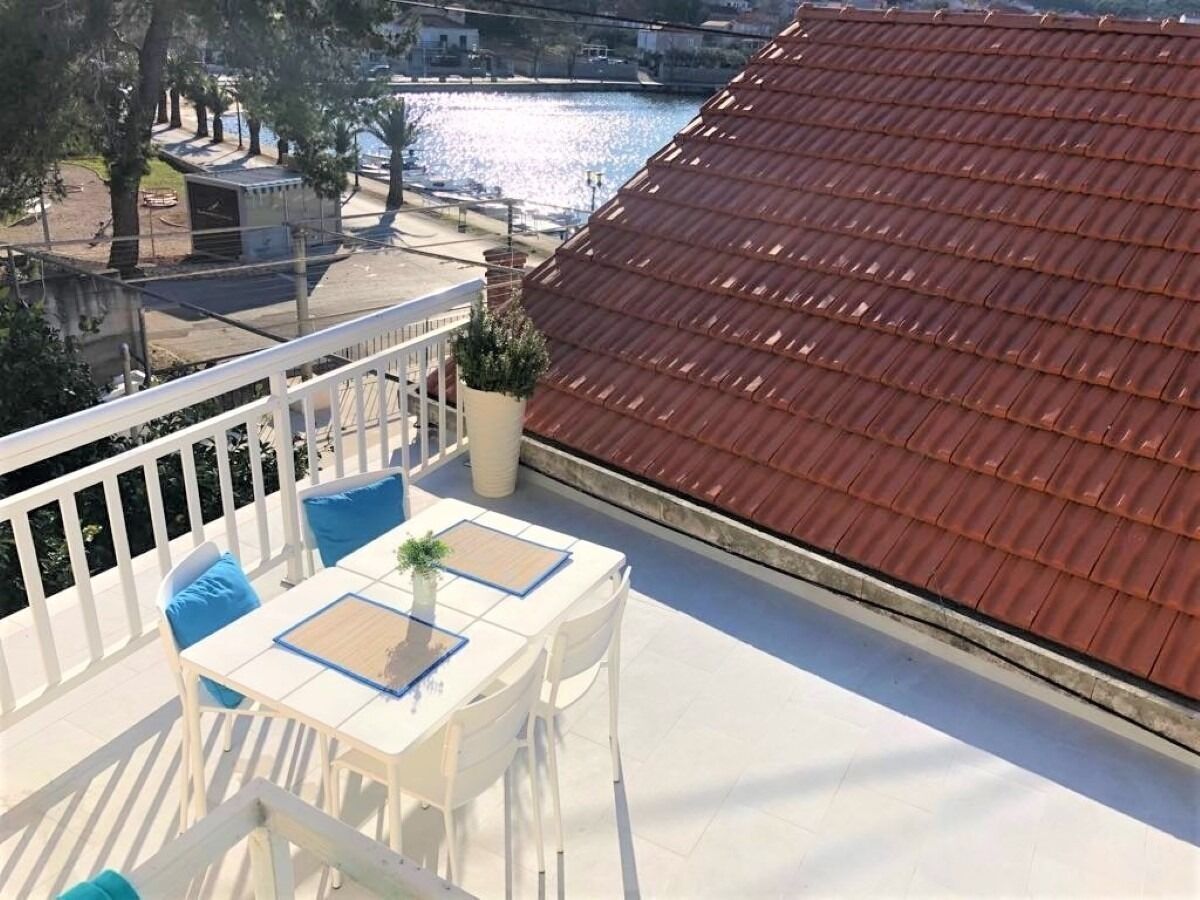 En balkon med et hvidt bord og stole, en potteplante og udsigt til en flod og bygninger.