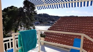 Un balcón con toldo azul a rayas, vista a un río y tejado de tejas rojas.