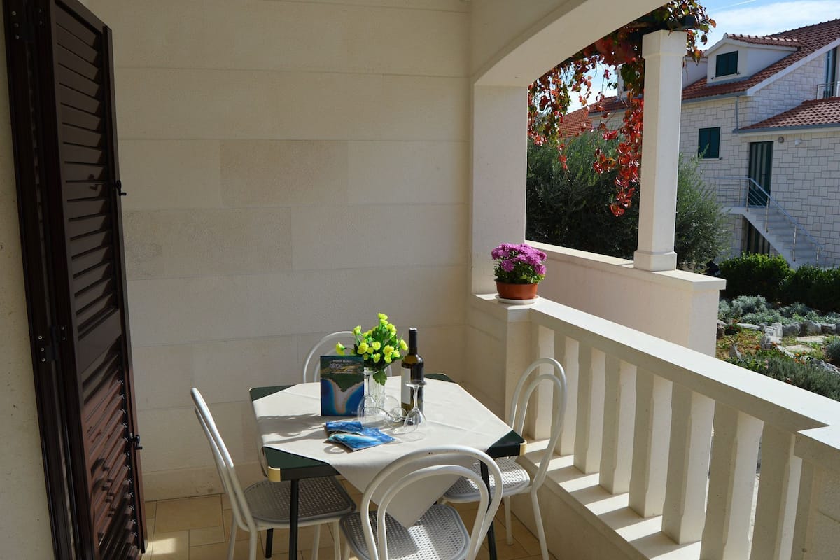 A balcony with a table set for two, chairs, a potted plant, and a view of the surrounding buildings.