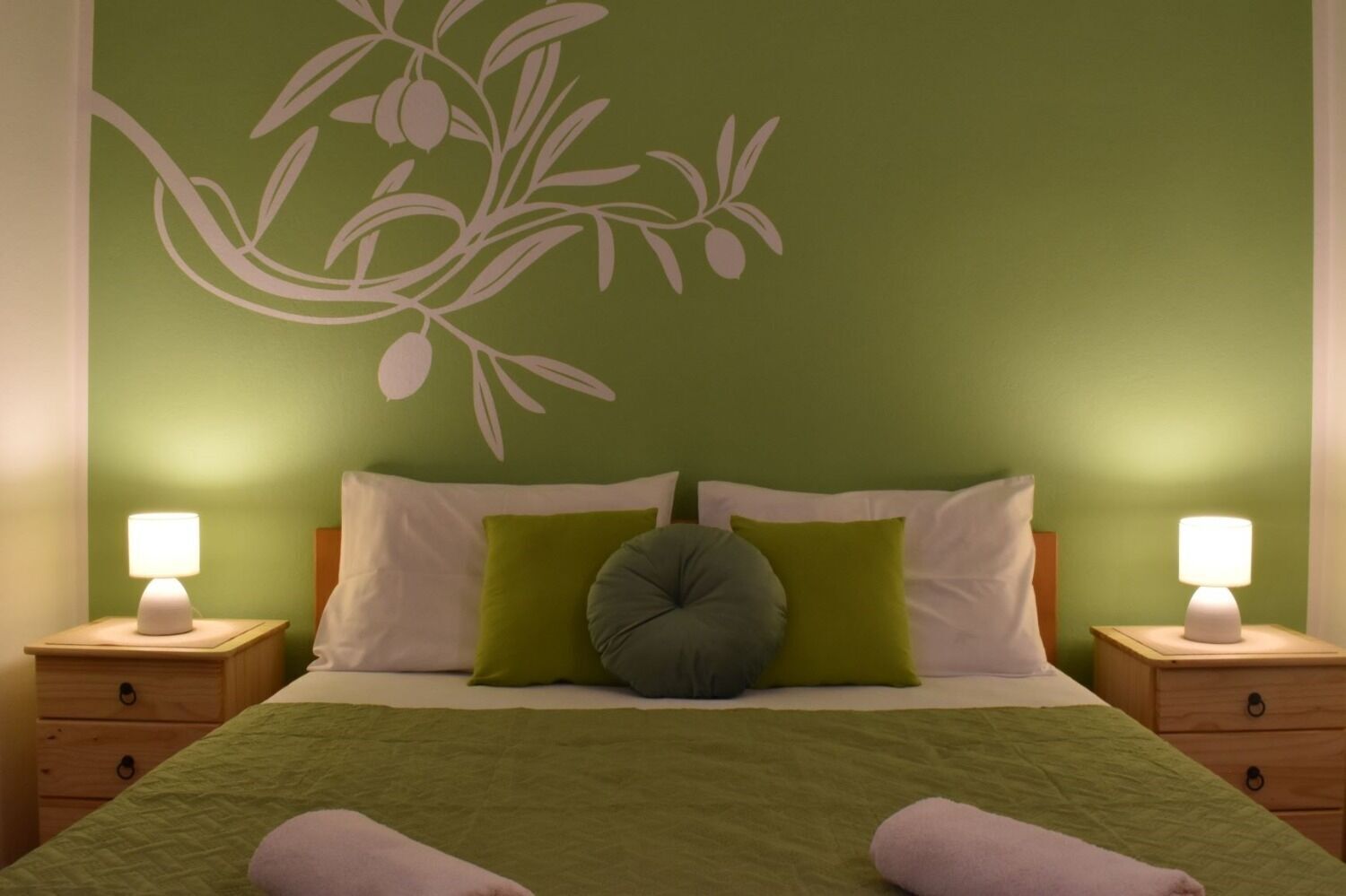 A neatly made bed with green bedding, two pillows, and two bedside lamps.