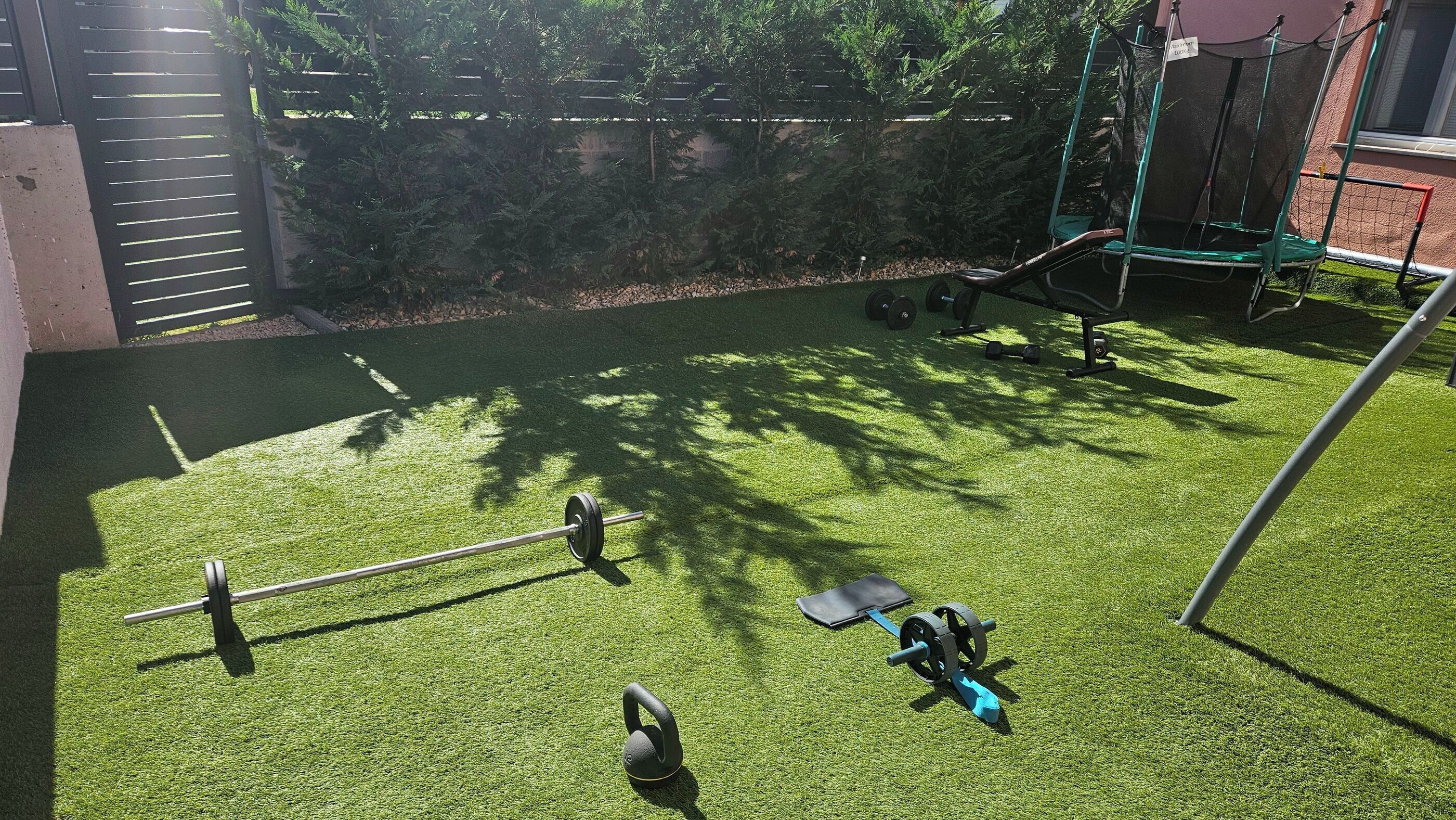 An outdoor exercise area with a pull-up bar, kettlebells, and a weight bench.