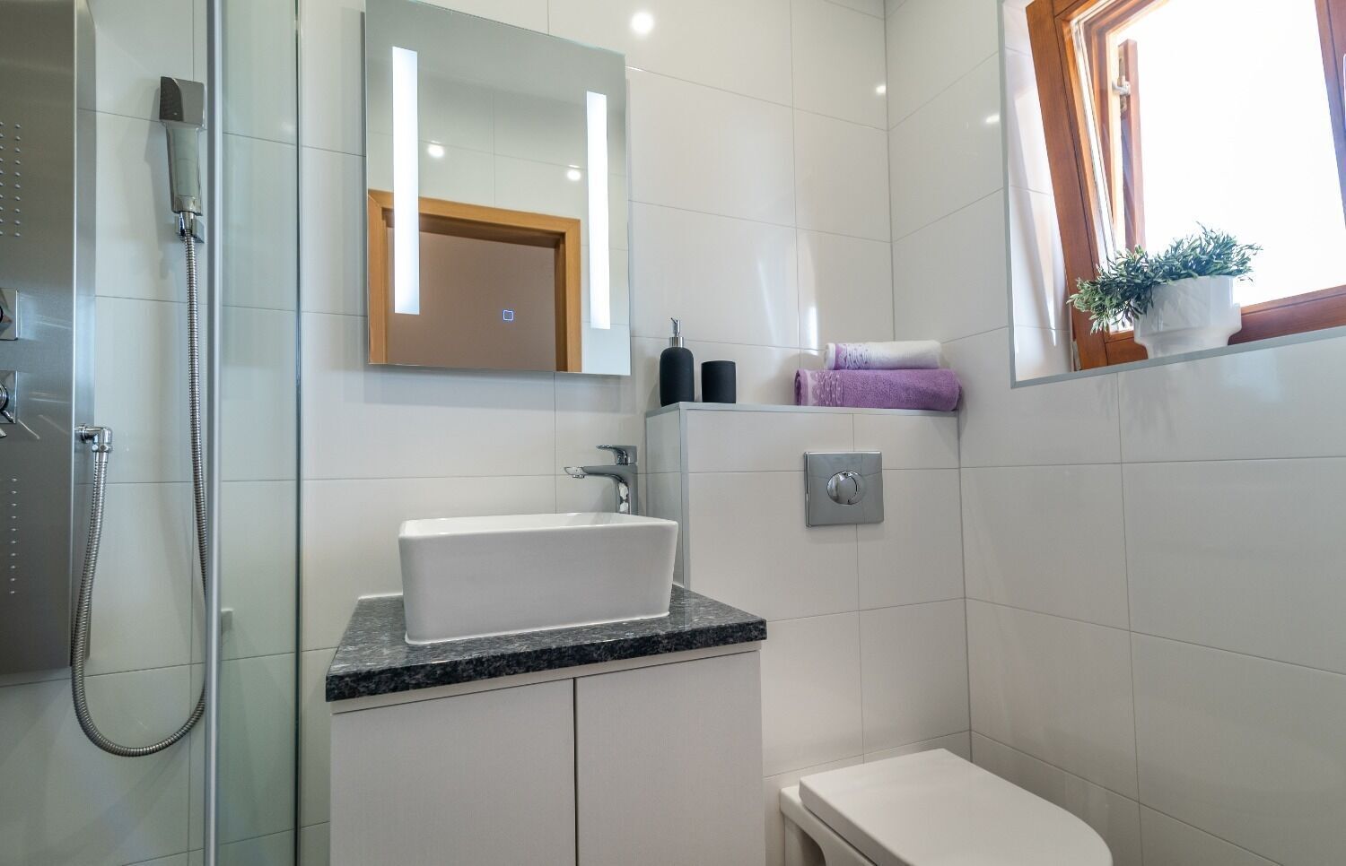 Ein modernes Badezimmer mit einer gläsernen Dusche, einem weißen Waschbecken mit Marmorplatte und einer Toilette.