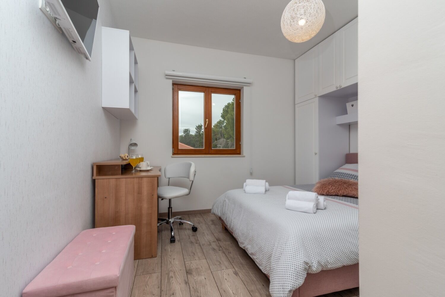 A compact bedroom with a bed, a desk, a chair, and a small bench.