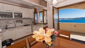 Een moderne keuken met witte kasten, een eettafel met stoelen en uitzicht op de zee door een groot raam.