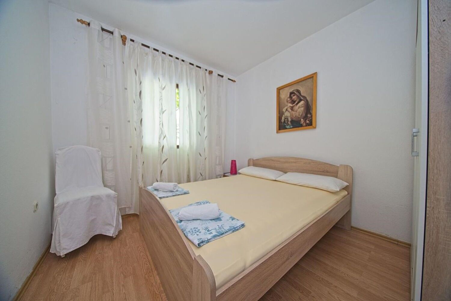Une chambre à coucher avec un lit, une chaise, un tableau et une fenêtre avec des rideaux.