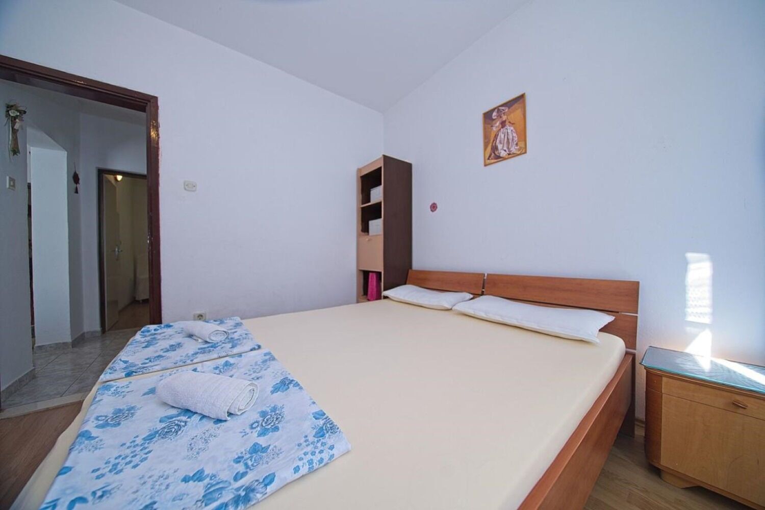 A bedroom with a bed, a wooden nightstand, a wardrobe, and a painting on the wall.